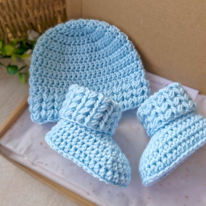 Set of blue crocheted baby hat and booties set on a light surface.