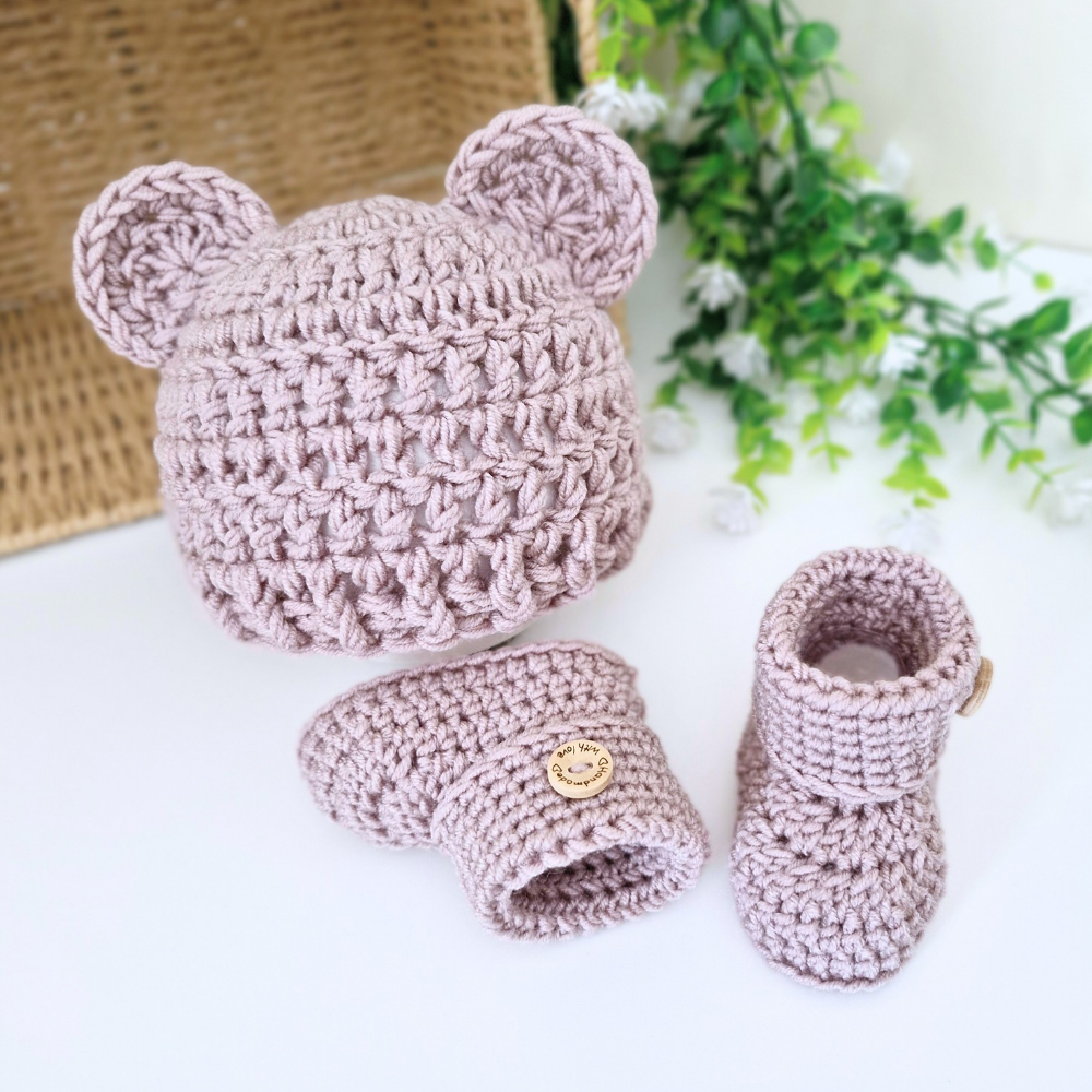 A crocheted baby teddy ear hat and bootie set in a dusty mauve-pink color.