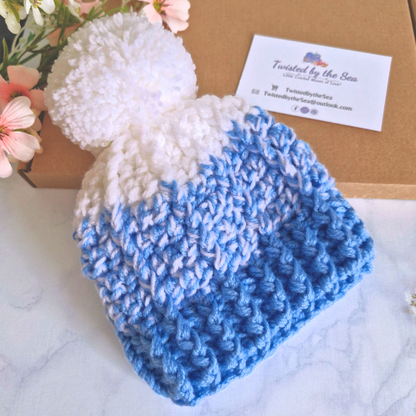 Blue and white crochet newborn hat with a business card on a floral background