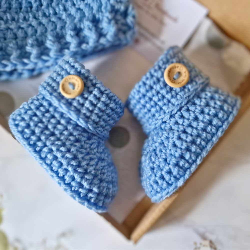 Pair of blue knitted baby booties with wooden buttons on a light background
