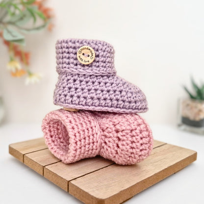 Crocheted baby booties in  on a wooden block with a blurred backgroundink and purple