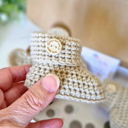 Close up of Handmade crochet baby bootie held by a hand with a blurred background in parchment