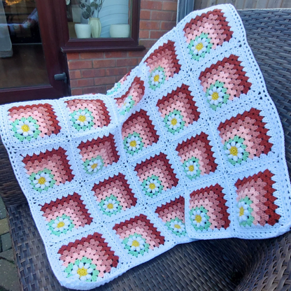 Handmade floral daisy crochet baby blanket in peach, green, and white draped over a chair - Twisted by the Sea 