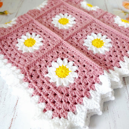Pink crocheted blanket with white daisy flowers on a wooden surface