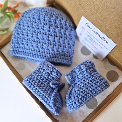 Blue crocheted baby hat and booties set with care instructions on a box.
