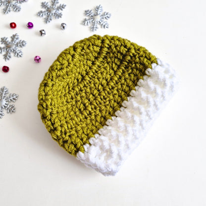 A hand-crocheted beanie hat with a textured olive green body and a white cuff, styled on a white background with silver snowflakes and small decorative beads.