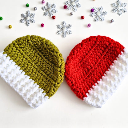 Two crocheted knit hats on a white background with holiday decorations. One hat is olive green and white, and the other is red and white, styled with silver snowflakes and small metallic beads.