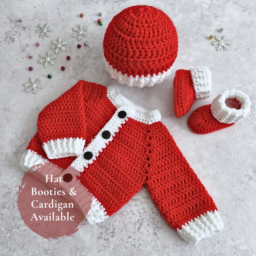 A crocheted baby outfit set laid flat on a light textured surface, including a red and white hat, matching booties, and a red cardigan with white trim and black buttons. Small decorative snowflake and bead props are scattered around, and a pink circle overlay reads 'Hat Booties & Cardigan Available'.