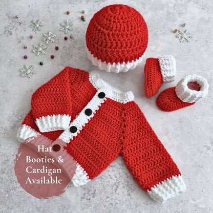A crocheted baby outfit set laid flat on a light textured surface, including a red and white hat, matching booties, and a red cardigan with white trim and black buttons. Small decorative snowflake and bead props are scattered around, and a pink circle overlay reads 'Hat Booties & Cardigan Available'.