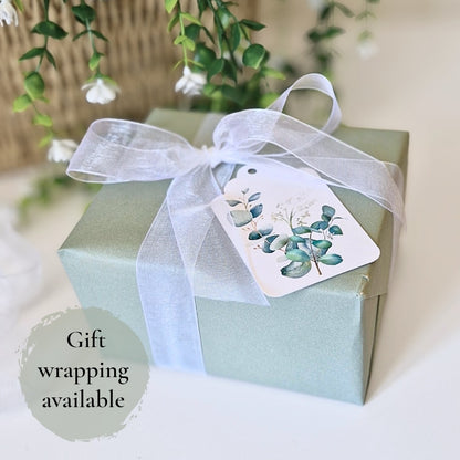 Gift box with a white ribbon and eucalyptus-themed tag on a light background showing that gift wrapping is avaliable 