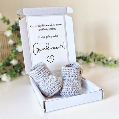 Crocheted baby booties in a box with a card for grandparents on a light background