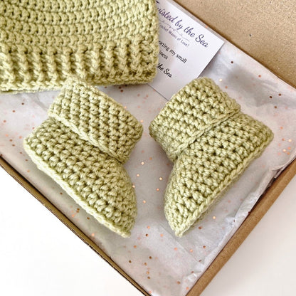 Green knitted baby booties on a box with a label