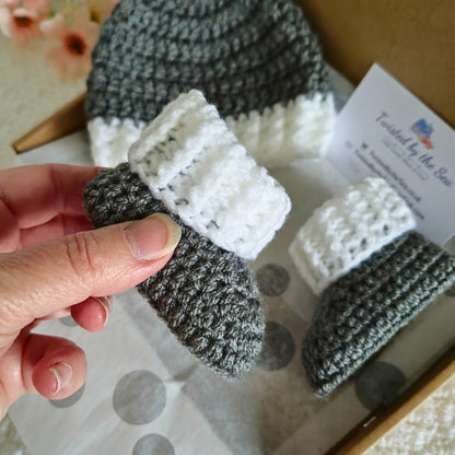 Hand holding a crochet baby bootie  with a box of similar items in the background