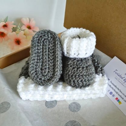 Crocheted gray and white baby booties on a white surface with a blurred background