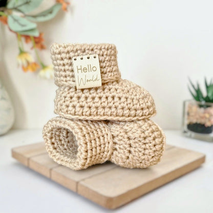 Stack of crocheted baby booties with a 'Hello World' tag on a wooden board.