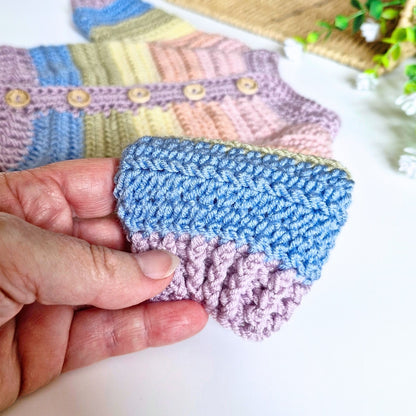 A close-up of a hand holding a crocheted baby cardifan sleeve. 