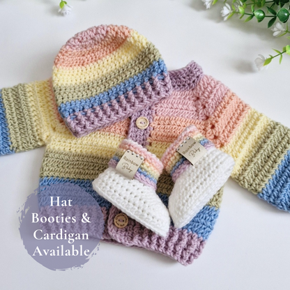 A handmade crocheted baby outfit set featuring a striped hat, cardigan, and booties in pastel rainbow colors, arranged on a white surface with a decorative text overlay.