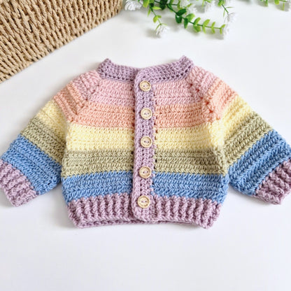 A handmade crocheted rainbow baby cardigan sweater, featuring horizontal pastel stripes in pink, yellow, green, blue, and purple, with a button-up front and wooden buttons, displayed on a white surface.