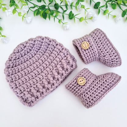 Set of purple crocheted baby hat and booties with button details on a white background.