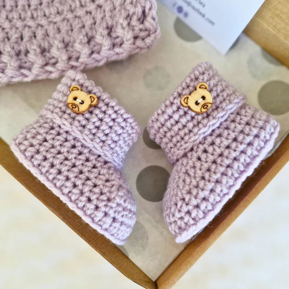 Heather purple crochet baby bootees with teddy bear buttons in a gift box