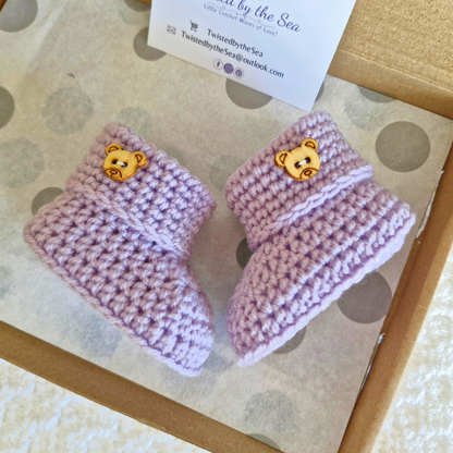 Handmade lavender crochet baby booties with wooden teddy bear buttons in a gift box