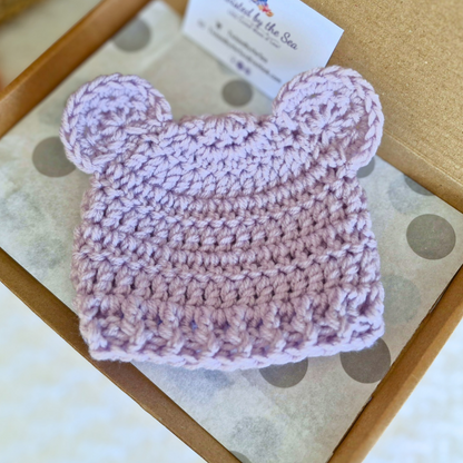 Heather lavender crochet teddy bear baby hat with round ears in a brown box on polka dot paper