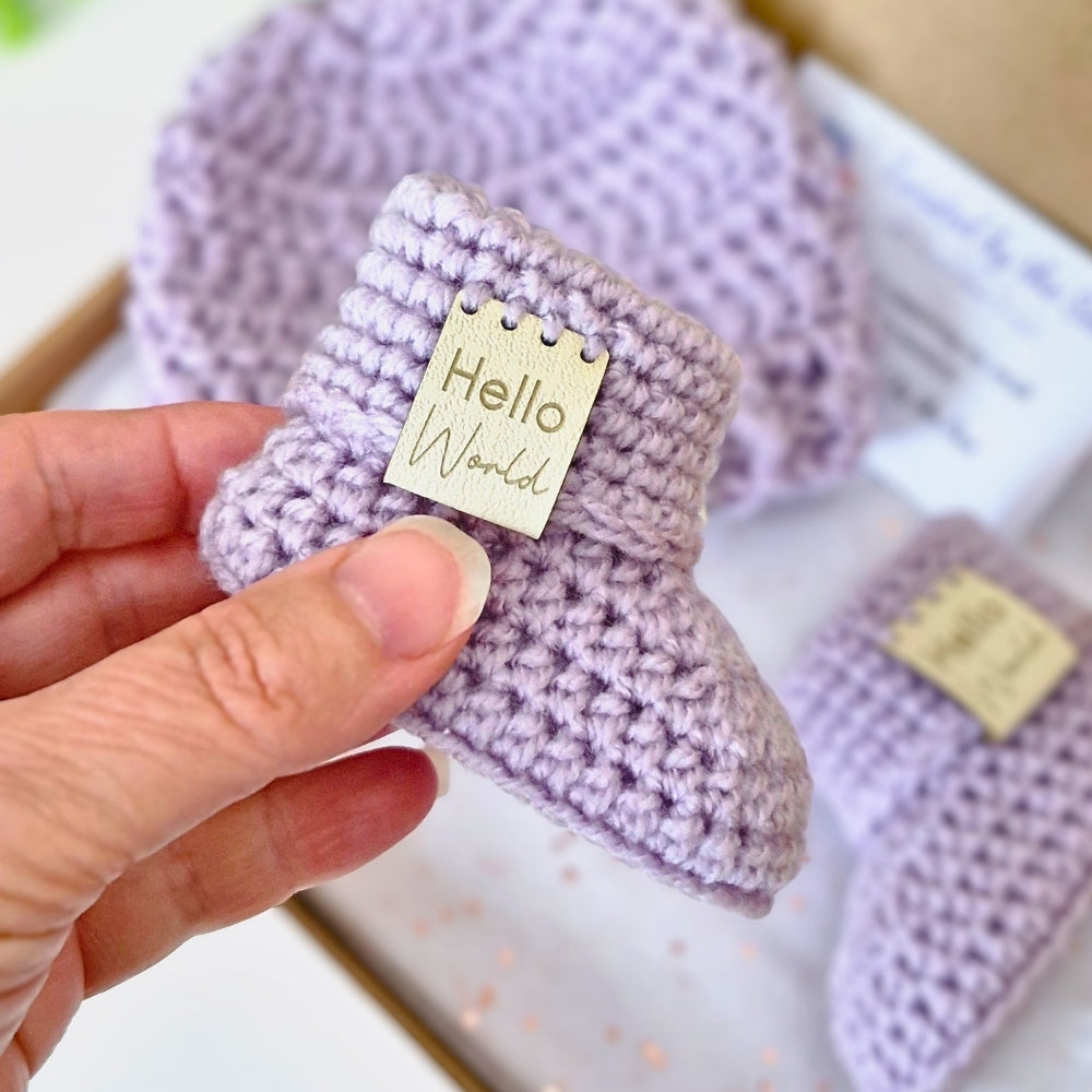 Purple baby booties with 'Hello World' tag held by a hand