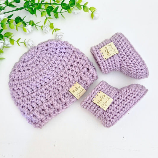 Purple crocheted baby hat and booties with 'Hello World' tags on a white background.
