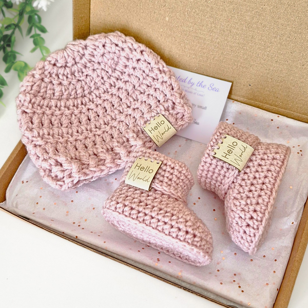 Pink crochet baby hat, booties set with 'hello world' tags in a box.