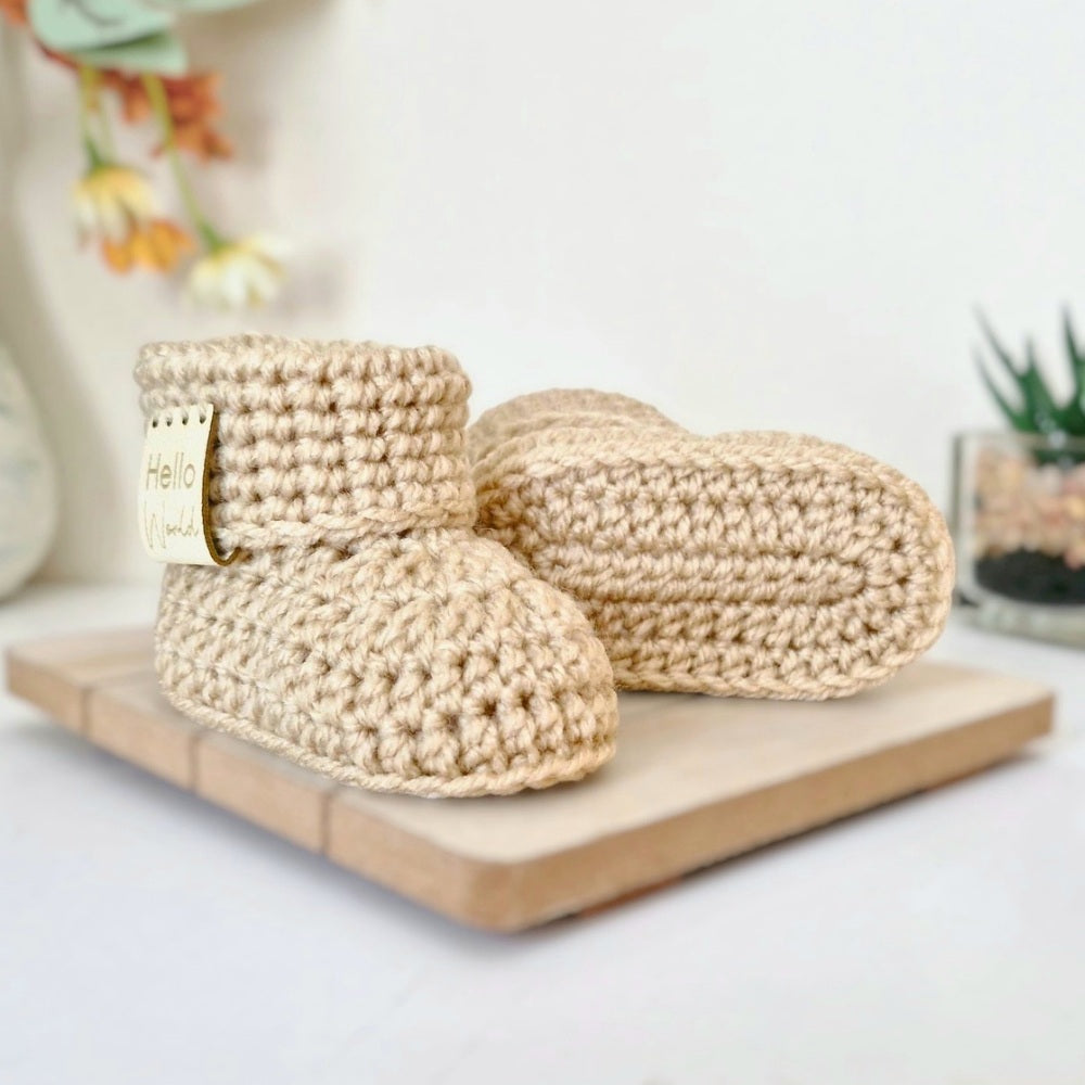 Pair of beige crochet baby booties on a wooden board with a blurred background