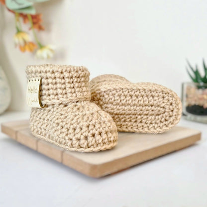 Pair of beige crochet baby booties on a wooden board with a blurred background