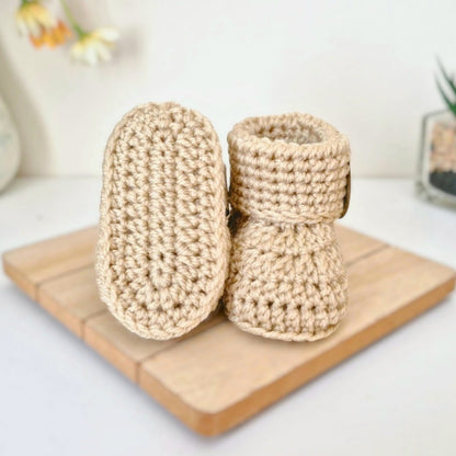Pair of beige crochet baby booties on a wooden surface with a blurred background