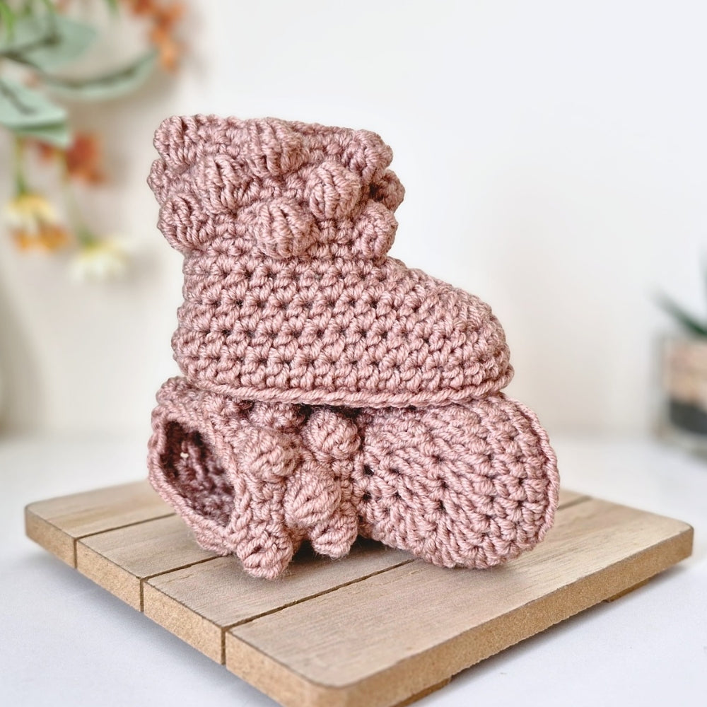 Pink crochet baby booties on a wooden surface with a blurred background