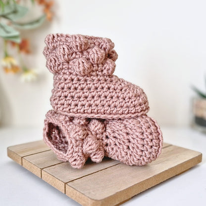 Pink crochet baby booties on a wooden surface with a blurred background