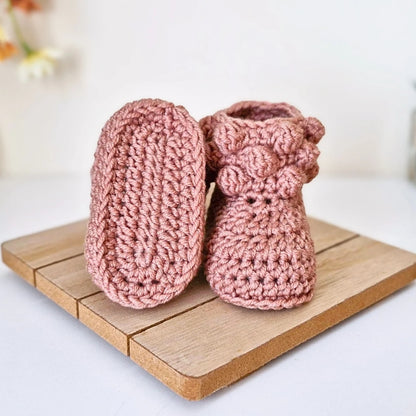 Pair of pink crochet baby booties on a wooden surface with a blurred background