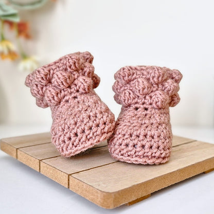 Pair of pink knitted baby booties on a wooden surface with a blurred background