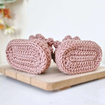 Pair of pink knitted shoes on a wooden board with a blurred floral background