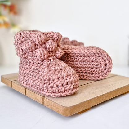 Pair of pink knitted baby booties on a wooden surface with a blurred background