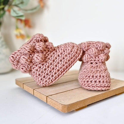 Pink knitted baby booties on a wooden board with a blurred background
