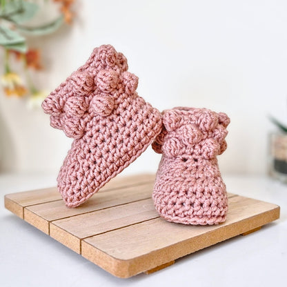 Pair of pink crochet baby booties on a wooden surface with a blurred background