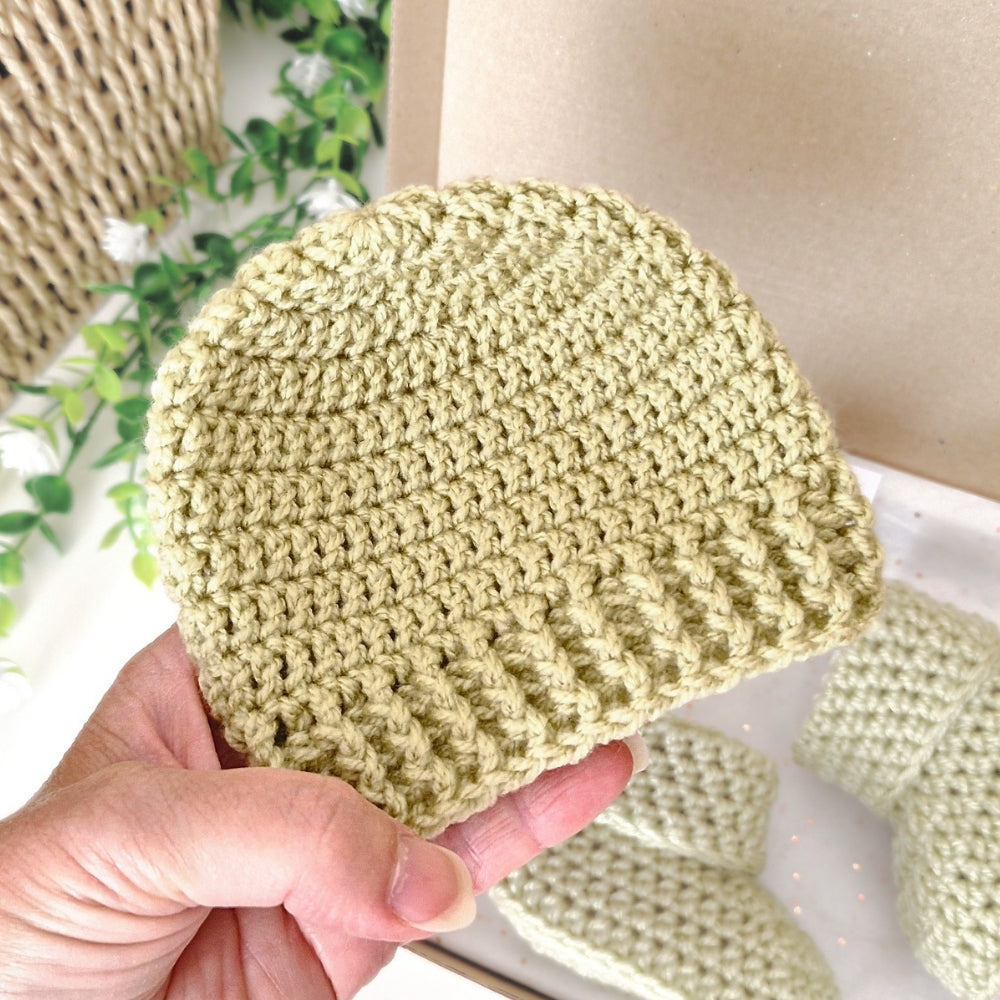 Hand holding a light mushy peas green crochet beanie 