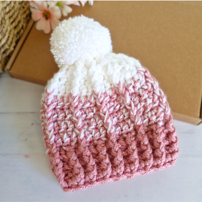 Pink and white crocheted beanie with a pom-pom on a light wooden surface.