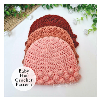 Three crocheted baby hats in stacked rows on a white background with decorative green leaves and white flowers. A white circular label reads 'Baby Hat Crochet Pattern' and 'Twisted by the Sea' appears near the bottom right.