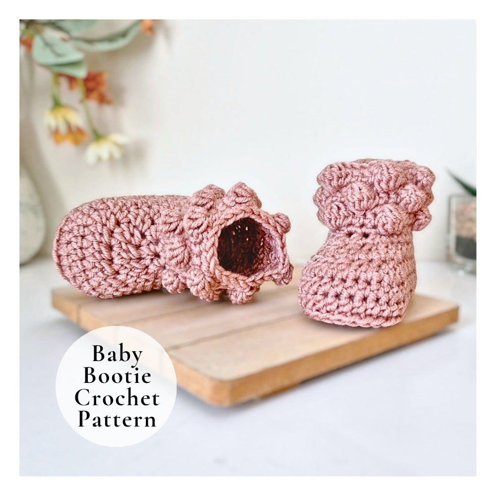Pink crochet baby booties on a wooden board with a blurred floral background