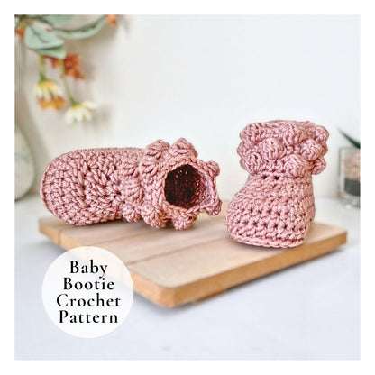 Pink crochet baby booties on a wooden board with a blurred floral background