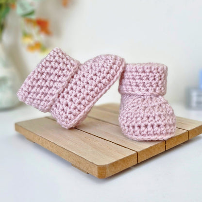 Wild orchid pale Pink crochet baby booties on a wooden stand with a blurred background