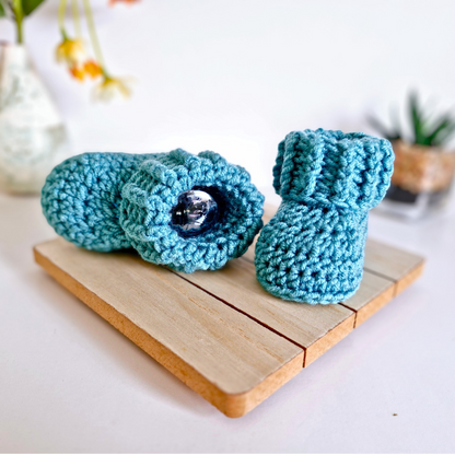 Pair of blue crochet baby booties on a wooden board with a blurred background