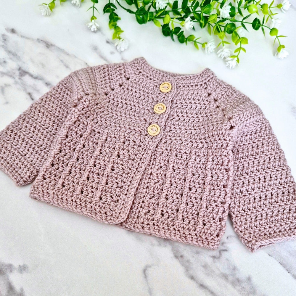 Mushroom crochet baby cardigan on a marble surface with greenery in the background