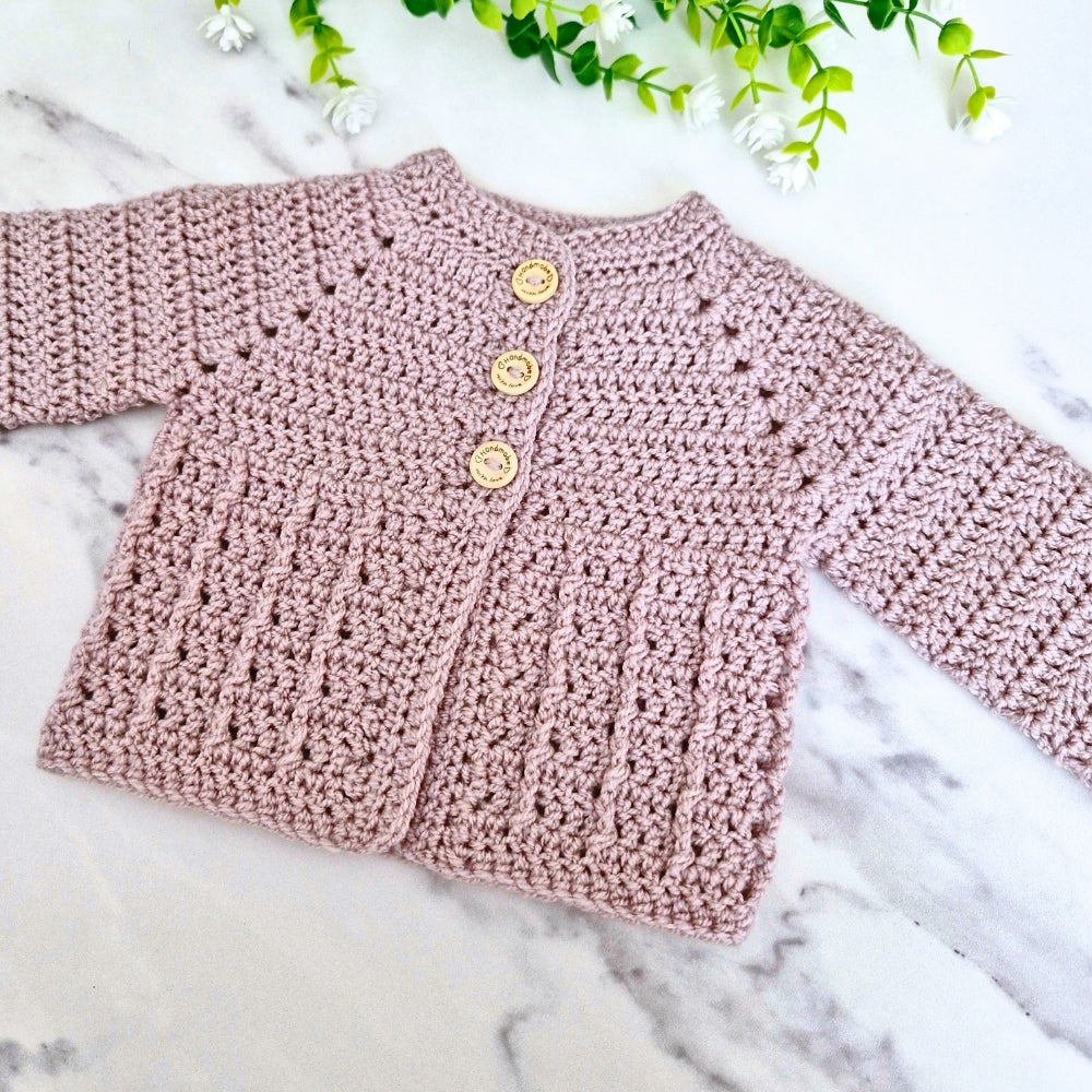 Neutral mushroom co.oured crochet baby cardigan with buttons on a marble surface