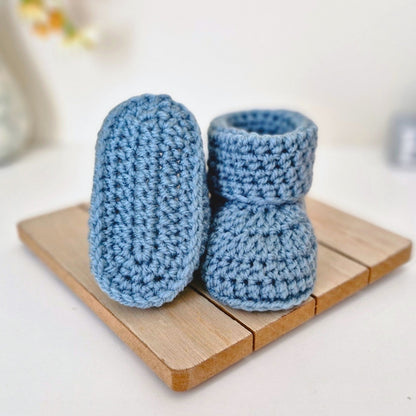 A pair of handmade blue crocheted newborn baby booties on a wooden surface.